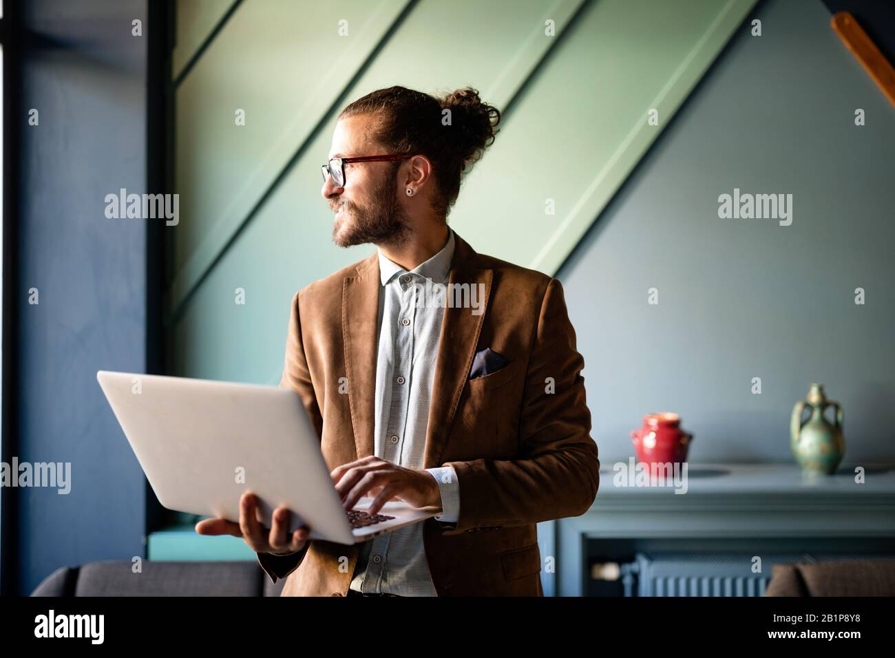 Glücklicher erfolgreicher Geschäftsmann, der mit einem Laptop im Büro arbeitet Stockfoto