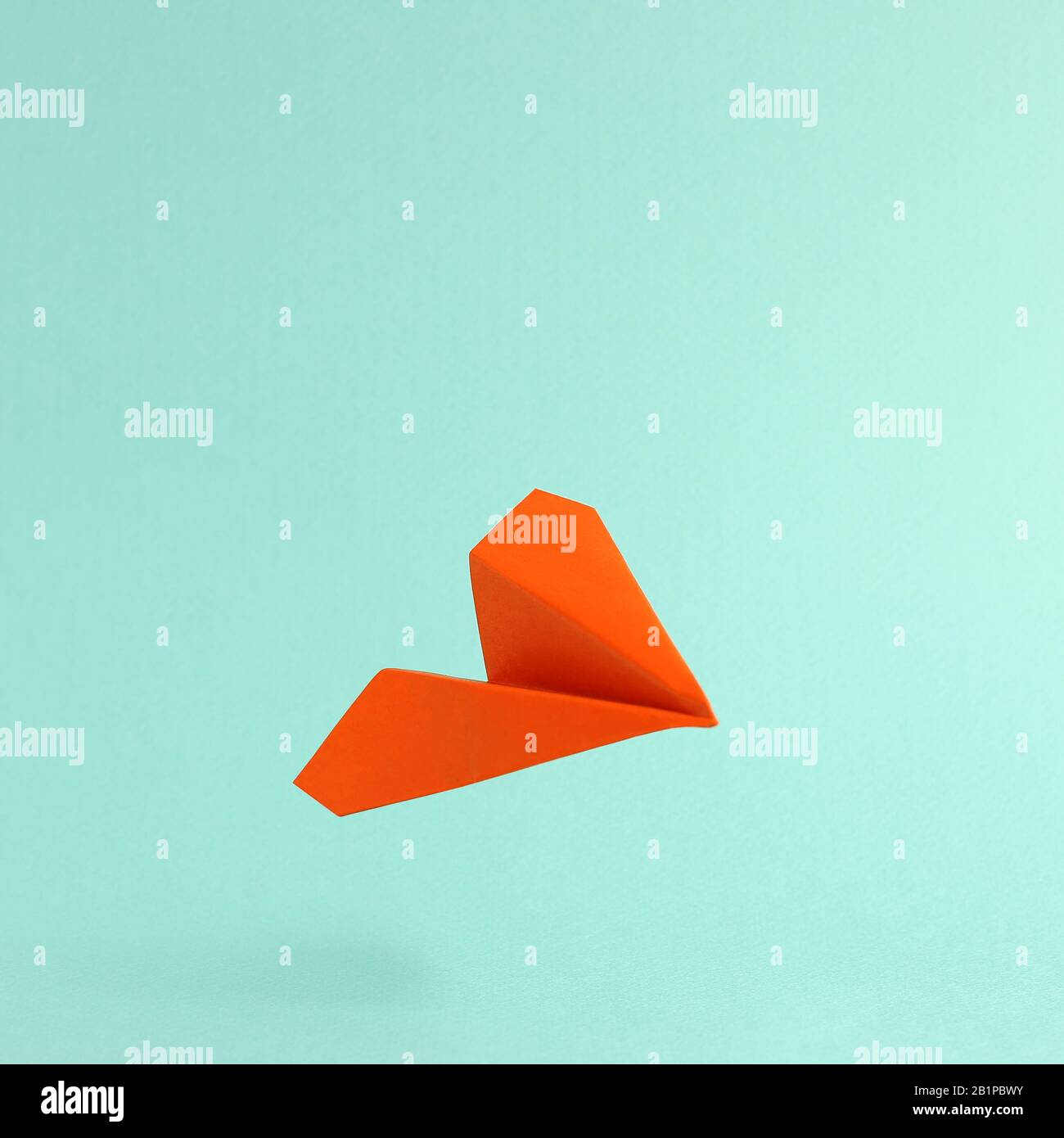 Orangefarbene Papierebene auf mintgrünem Hintergrund Stockfoto