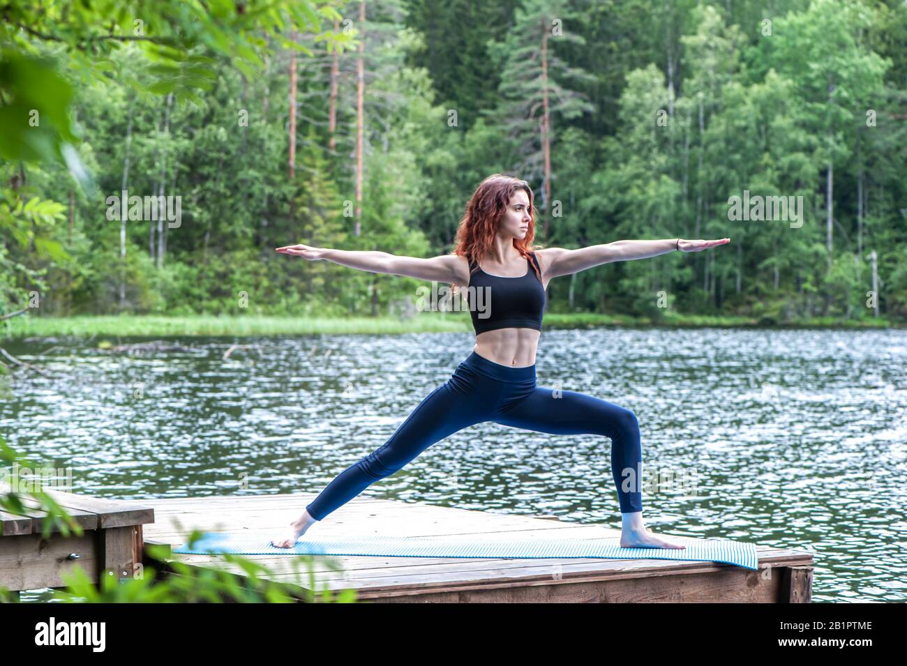 Junge yogi Mädchen üben Yoga, im Krieger zwei Übung stehend, Virabhadrasana II Pose auf dem See. Konzept des gesunden Lebens und der natürlichen Balance Stockfoto