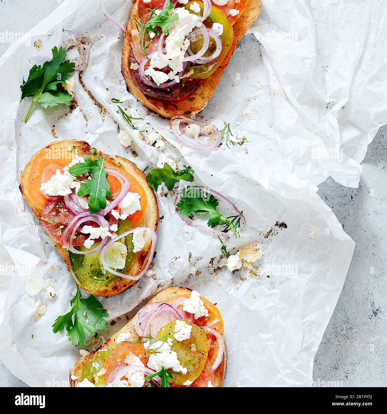 Italienische Bruschetta (Sandwich, Crostini, Tapas, Toast) mit frischen Tomaten, Ricotta, Kräutern, Zwiebeln, Olivenöl und Laub auf blauem Grund. Stockfoto