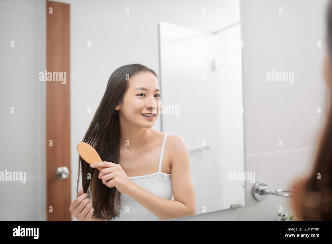 Fröhliche, attraktive junge Frau, die nach der Dusche zuhause nasses Haar mit Kamm im Bad kämmt. Haarpflege und gesundes Haar Stockfoto
