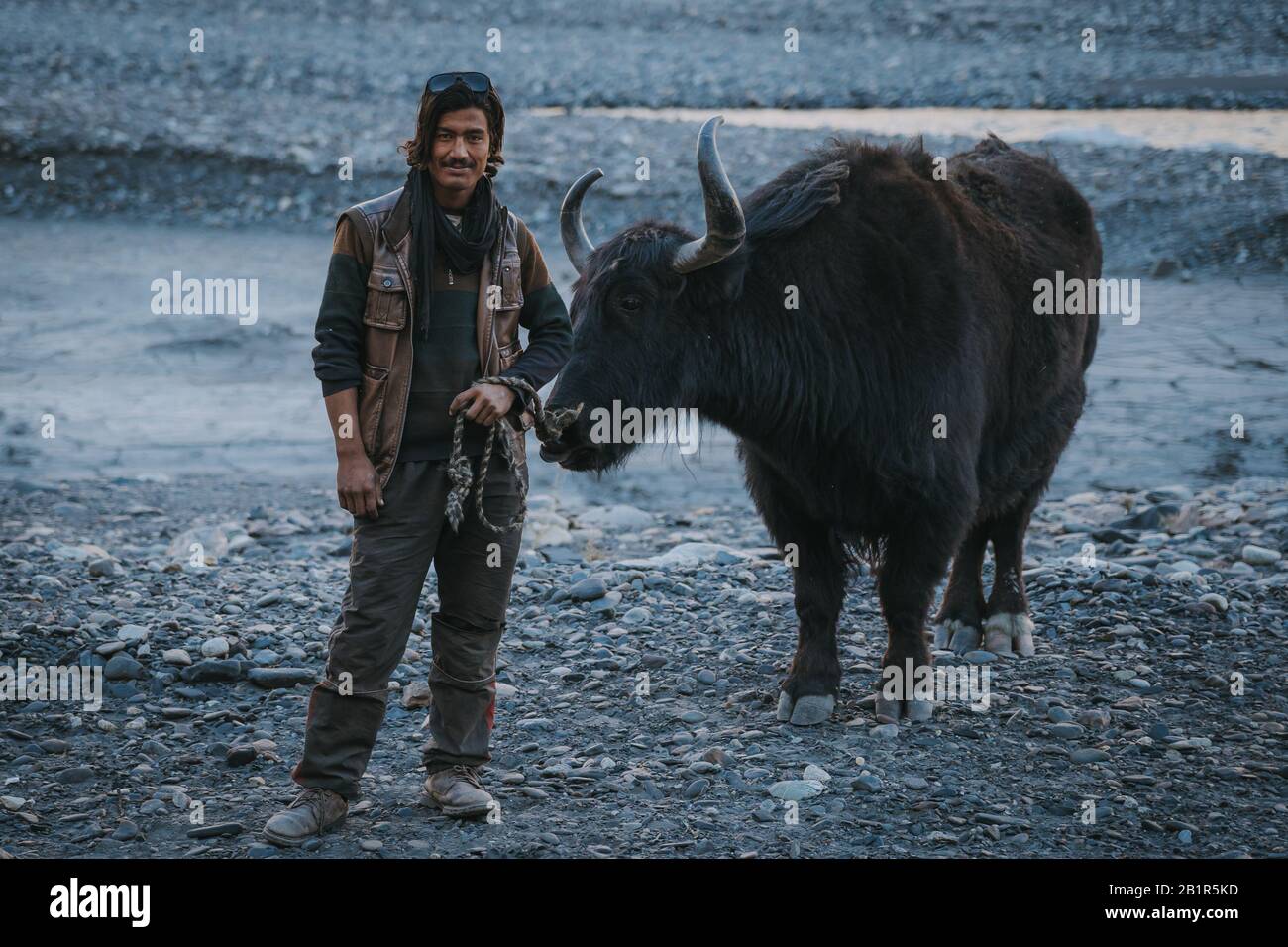 Sust, Pakistan - Oktober 2019: Herder in traditioneller Kleidung stehend mit seinem Yak im Pamir-Gebirge, Pakistan mit Blick auf die Kamera auf karger te te Stockfoto