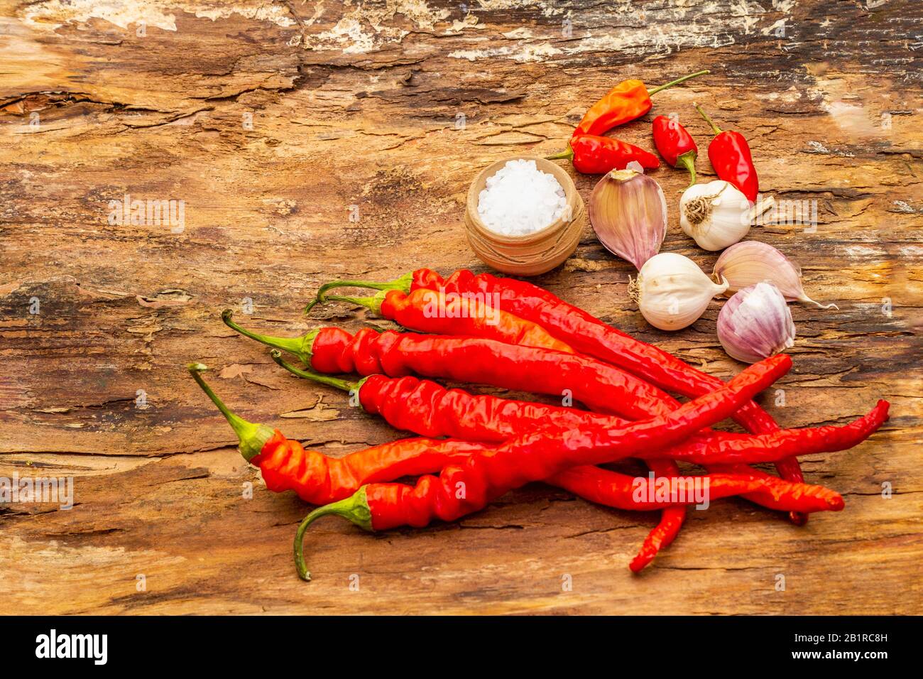 Rote und orangefarbene Chilischote mit Knoblauch-Kochgrund. Traditionelle Zutaten für die Zubereitung gesunder Speisen. Holzbarkenhintergrund, SEA sal Stockfoto