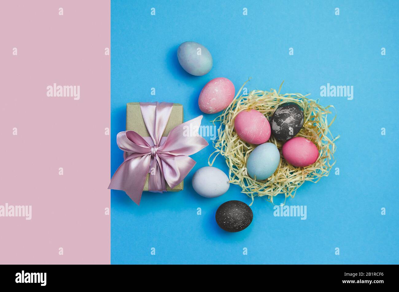 Ostereier und Nestlé mit bunten Eiern mit Geschenk auf pinkfarbenem und blauem Hintergrund Stockfoto