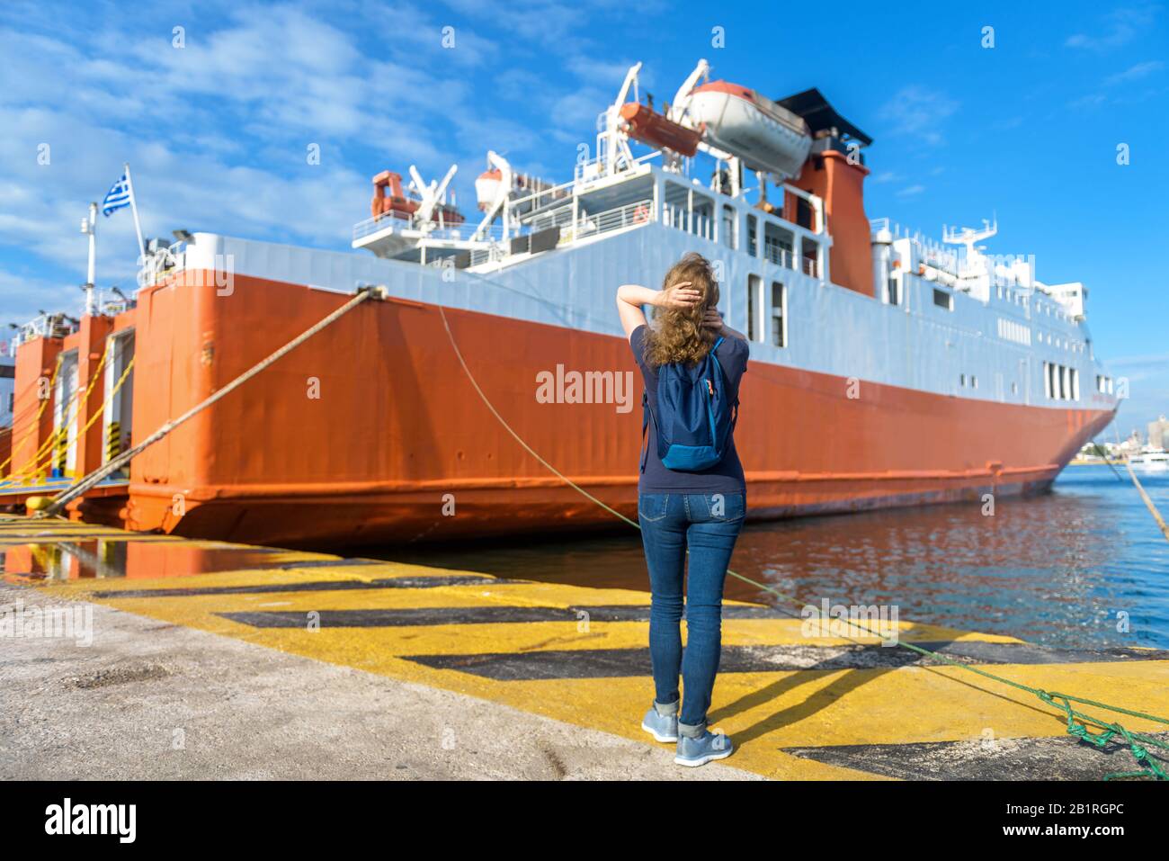 Junge Frau schaut auf Fährschiff im Hafen von Piräus, in der Nähe von Athen, Griechenland. Großes Schiff im Sommer im Seehafen angedockt. Autofähre zum Be- oder Entladen einer Stockfoto