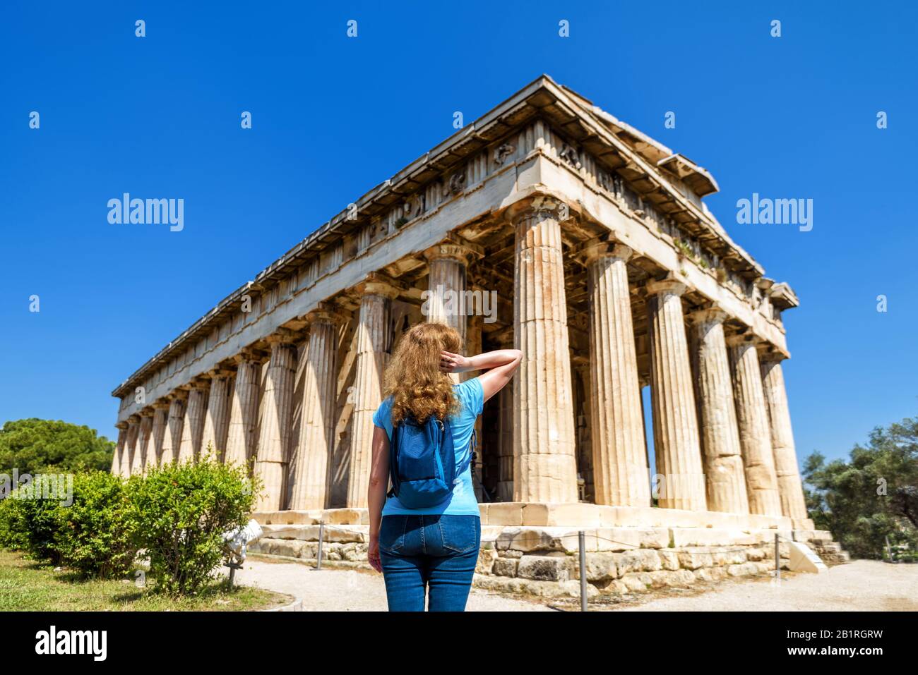 Junge Frau blickt auf den Tempel von Hephaestus, Athen, Griechenland. Diese altgriechische Struktur ist eines der Hauptmerkmale Athens. Touristen besuchen die Agora i. Stockfoto