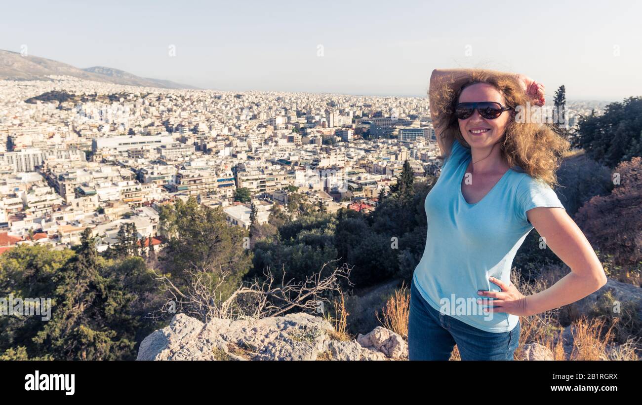 Junge hübsche Frau lächelt in Athens Stadt, Griechenland. Schöne weibliche Touristenpossen mit Blick auf Athen im Sommer. Attraktive glückliche Frau steht im Hintergrund Stockfoto