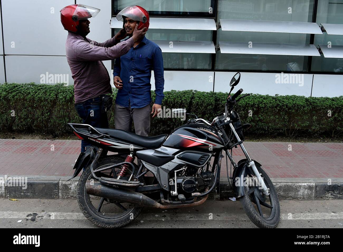 (200227) -- DHAKA, 27. Februar 2020 (Xinhua) -- Ein auf Apps basierender Motorradfahrer hilft einem Passagier, Helm zu tragen, bevor er am 27. Februar 2020 auf einer Straße in Dhaka, Bangladesch, fuhr. Die Motorraddienste mit Mitfahrerservice haben in Bangladeschs Hauptstadt Dhaka an Popularität gewonnen. (Str/Xinhua) Stockfoto