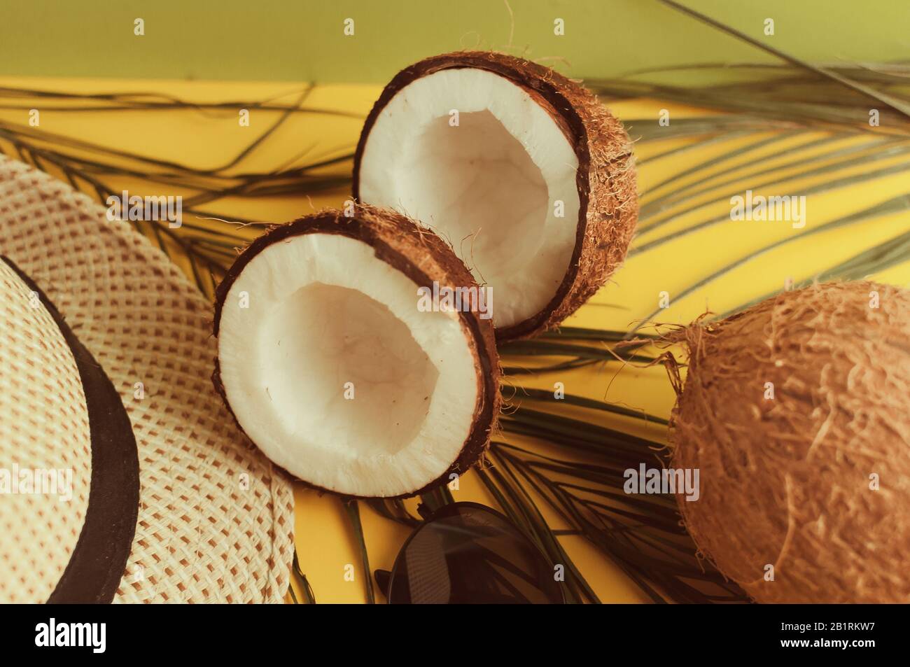 Sommerkomposition. Tropische Palmblätter, Hut, Brille und gebrochene Kokosnuss auf einem sandigen Hintergrund. Das Konzept der Sommersaison, Partys und Hitze Stockfoto