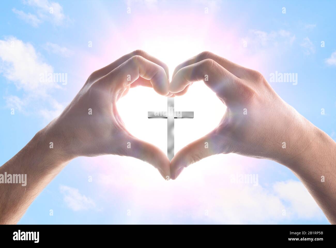 Hände eines Mannes, der ein Herz im Himmel bildet, mit Spitzen, die ein Kreuz umgeben. Horizontale Zusammensetzung Stockfoto