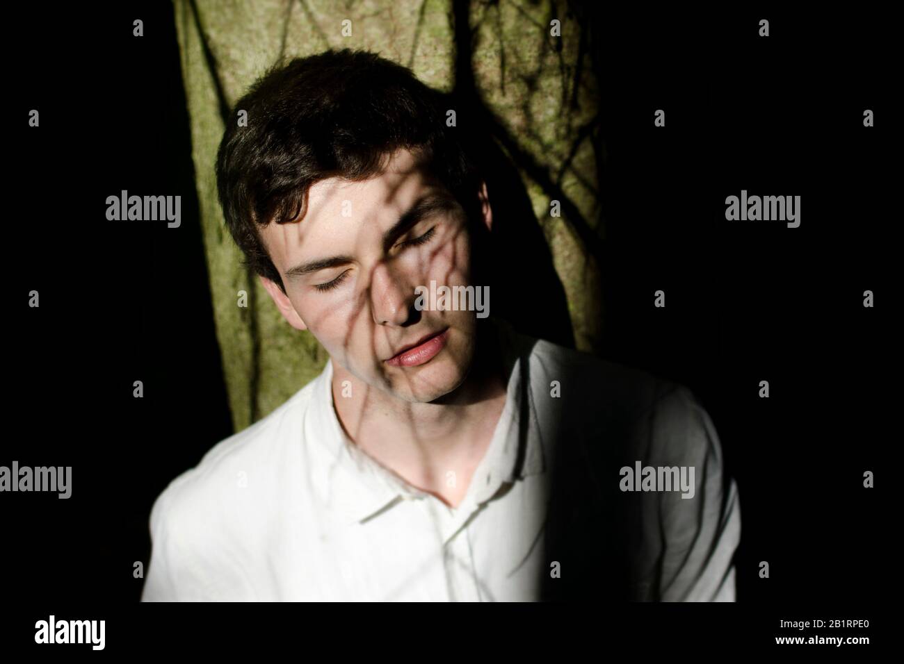 Junger Mann mit Schatten aus Ästen im Gesicht, Stockfoto