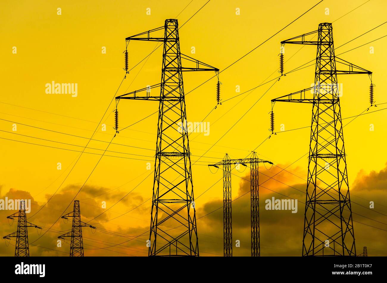 Energieübertragungstürme oder Elektrizitätspylone mit goldenem Himmel und Wolken Stockfoto