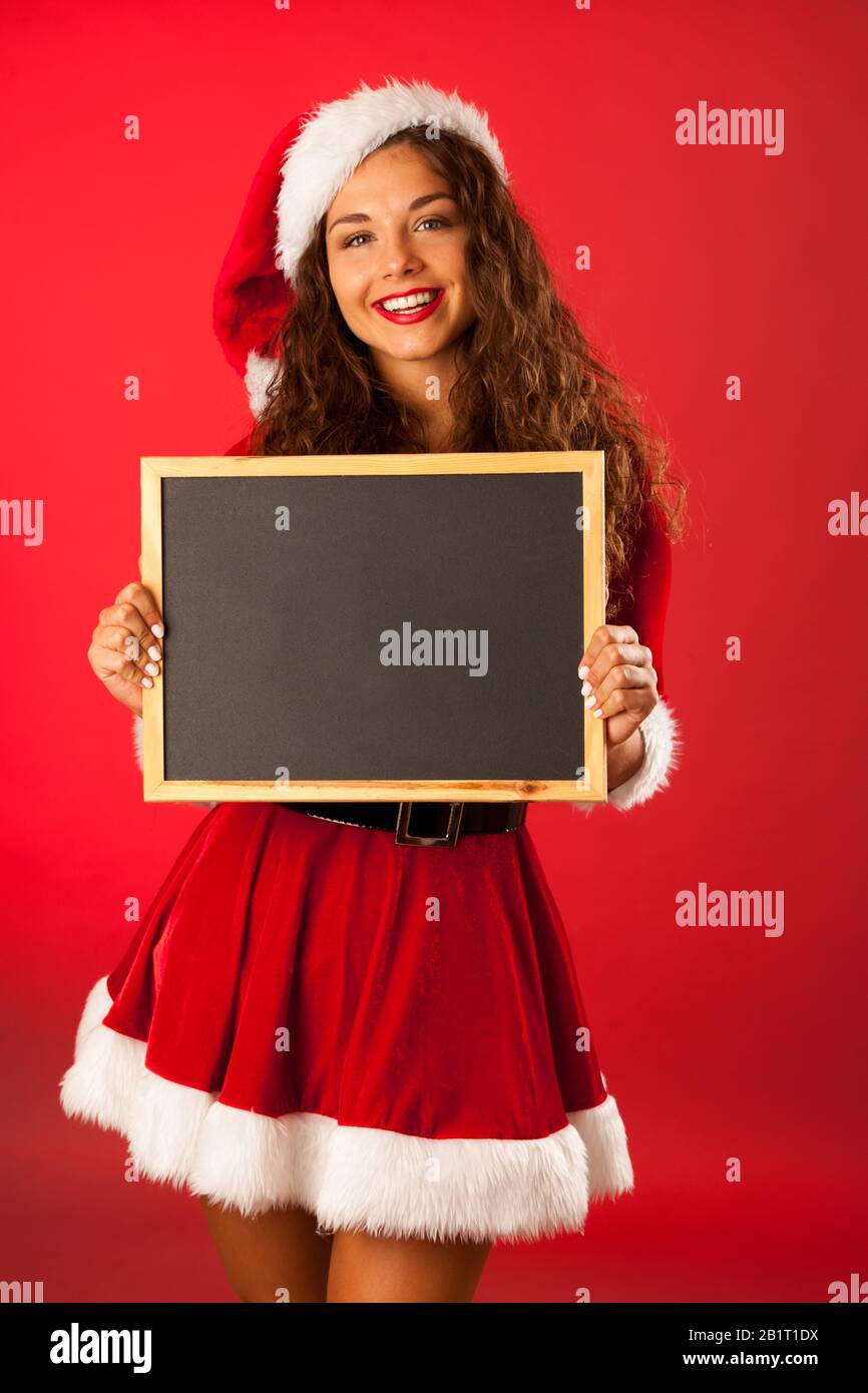 Schöne junge Frau in santa dres hält Tafel über rotem Hintergrund Stockfoto