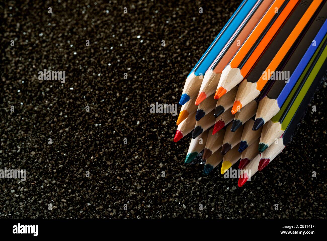 Gruppe von Bleistiften, die auf schwarzem Sand liegen. Bunte Bleistifte. Stockfoto