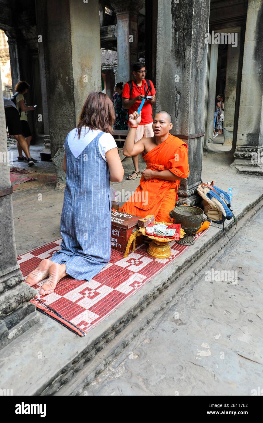 Ein buddhistischer Mönch, der mit orangefarbenen Gewändern bekleidet ist und einer Touristin im Angkor Wat Tempelkomplex, Siem Reap, Kambodscha, Asien, einen Segen gibt Stockfoto