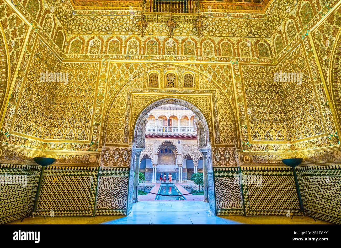 Sevilla, SPANIEN - 1. OKTOBER 2019: Die malerische prunkvolle Wand der Botschafterhalle mit bogenförmigem Eingang zum Innenhof des Maidens mit kleinem Pool, Stockfoto