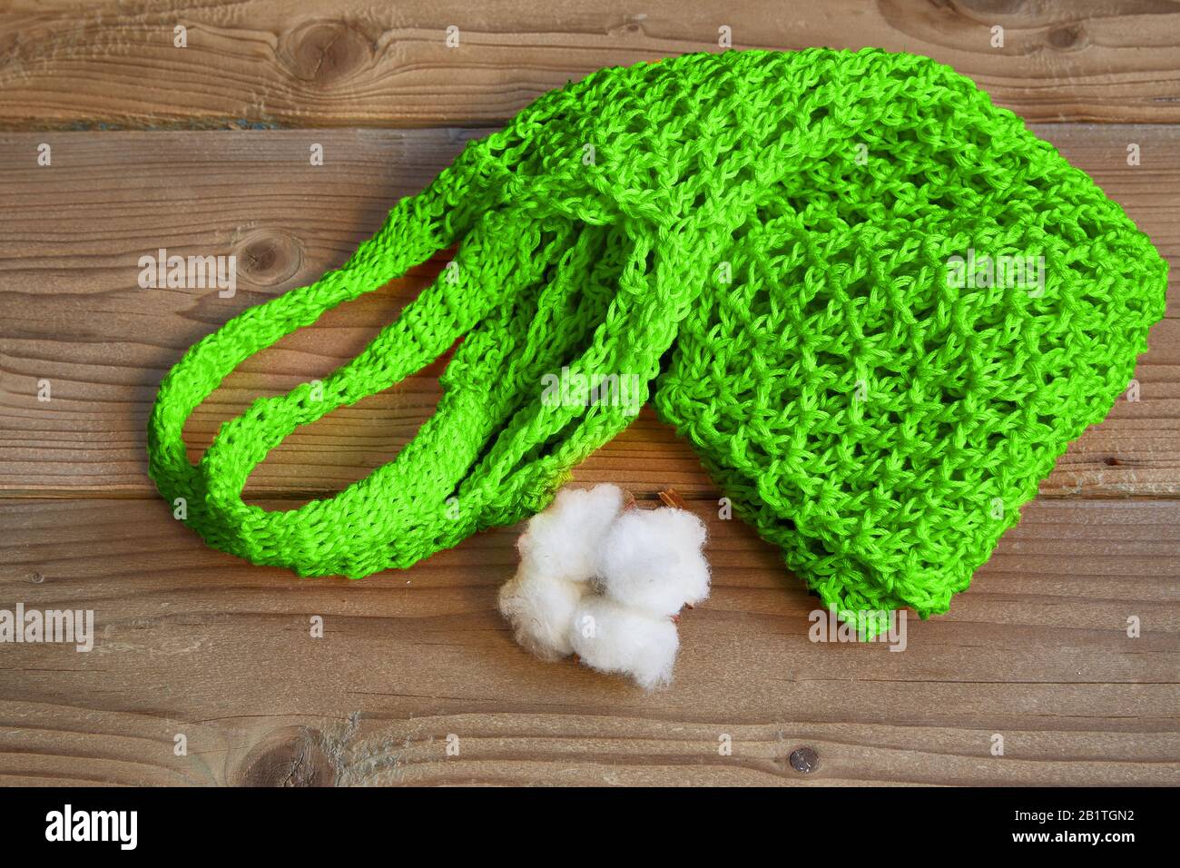 Grüne Saitenbeutel und baumwollboll liegen auf einem holzbraunen Hintergrund. Stockfoto