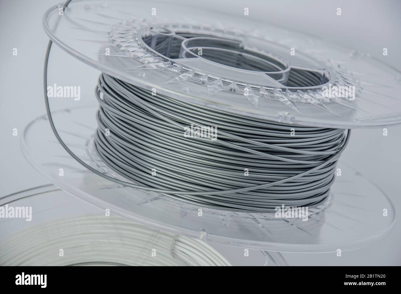 Nahansicht von Kunststoff für 3D-Druck. Silberfarbener Kunststofffilament, graue ABS/PLA-Spule für 3D-Drucker, isoliert auf weißem Hintergrund. Stockfoto