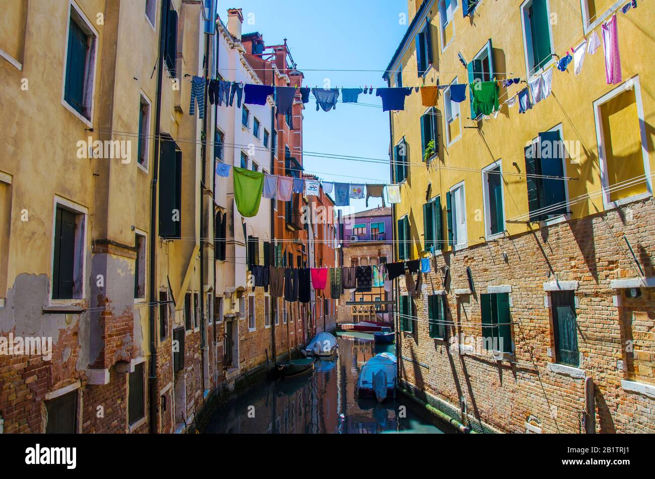 Wäscherei, die aus einer typisch venetianischen Fassade, Italien, hängt. Enge Kanalstraße mit bunten Gebäuden und Booten in Venedig und Kleidung trocken an einem Seil Stockfoto