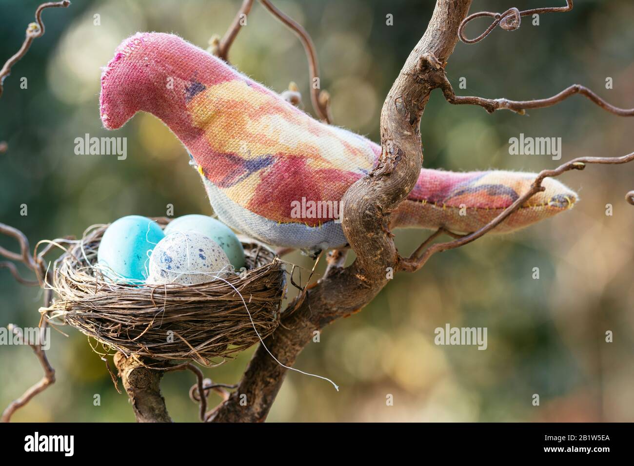Handgefertigter Vogel weich auf einem Zweig mit gefälschtem Nest. Stockfoto