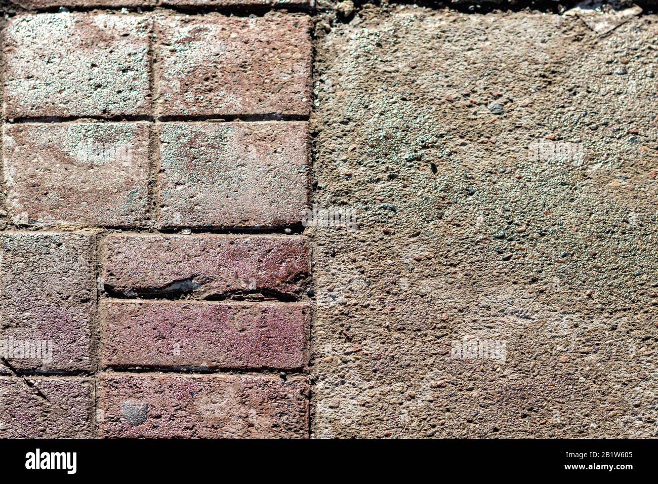 Eine nach oben oder oben liegende Ansicht eines Gehwegs zeigt den Übergang zwischen rauem, körnigem Gussbeton und verwitterten roten Backsteinen. Stockfoto