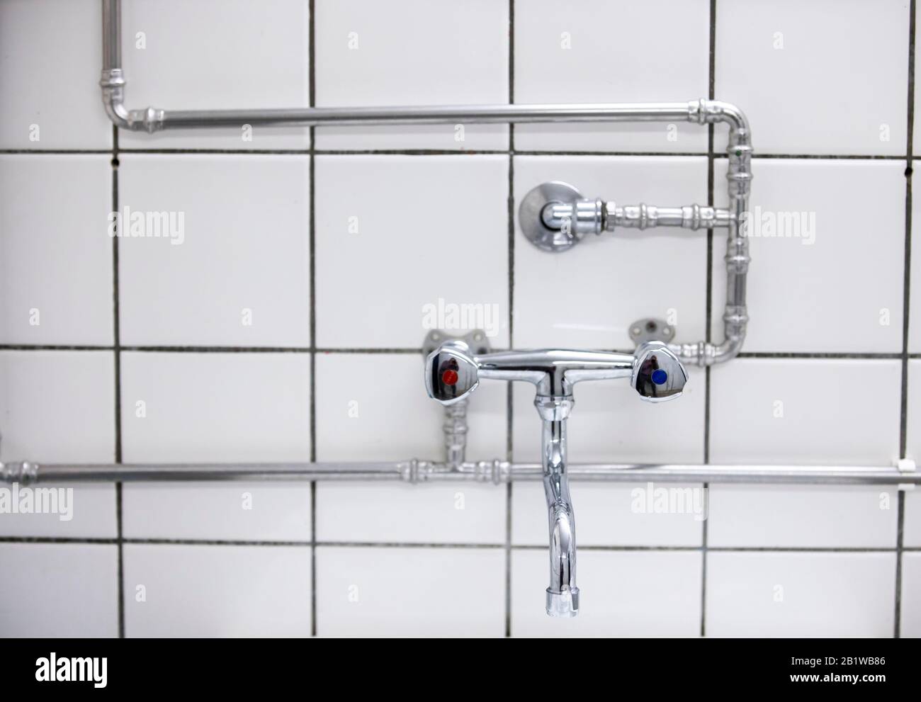 Wasserleitungen, für einen Wasserhahn, über die Fliesen gelegt, in einem Waschraum Stockfoto
