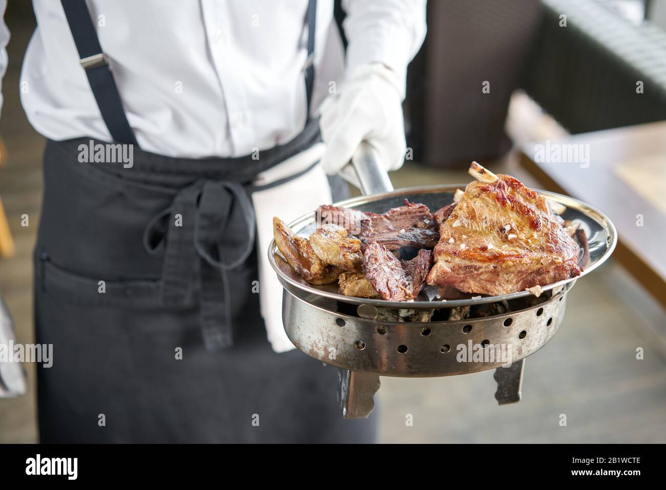 Der Kellner hält einen Teller Mit Verschiedenen gegrillten Fleischgerichten. Grillrestaurant Menü, eine Reihe von Fotos von verschiedenen Fleischsorten. Stockfoto