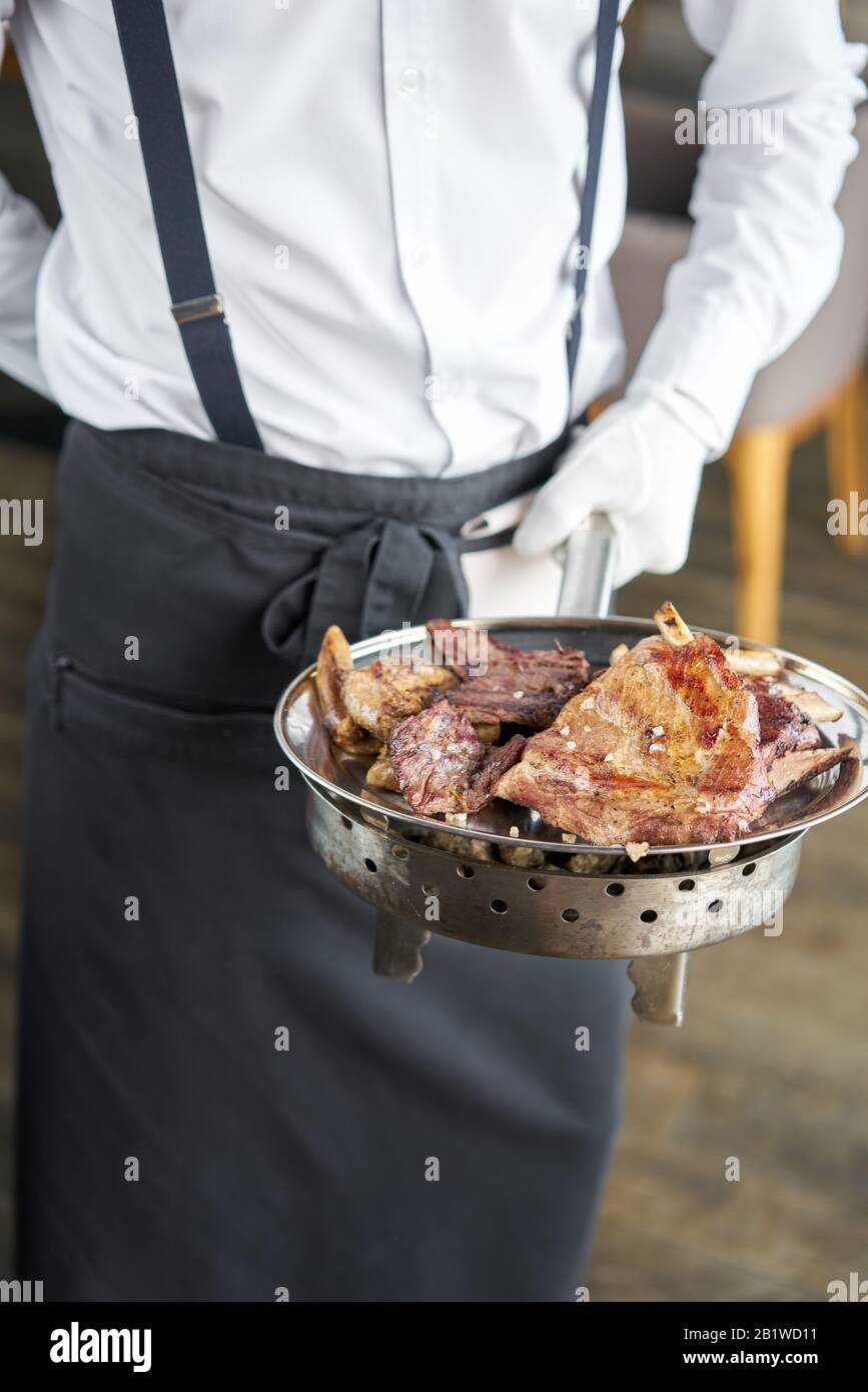 Der Kellner hält einen Teller Mit Verschiedenen gegrillten Fleischgerichten. Grillrestaurant Menü, eine Reihe von Fotos von verschiedenen Fleischsorten. Stockfoto