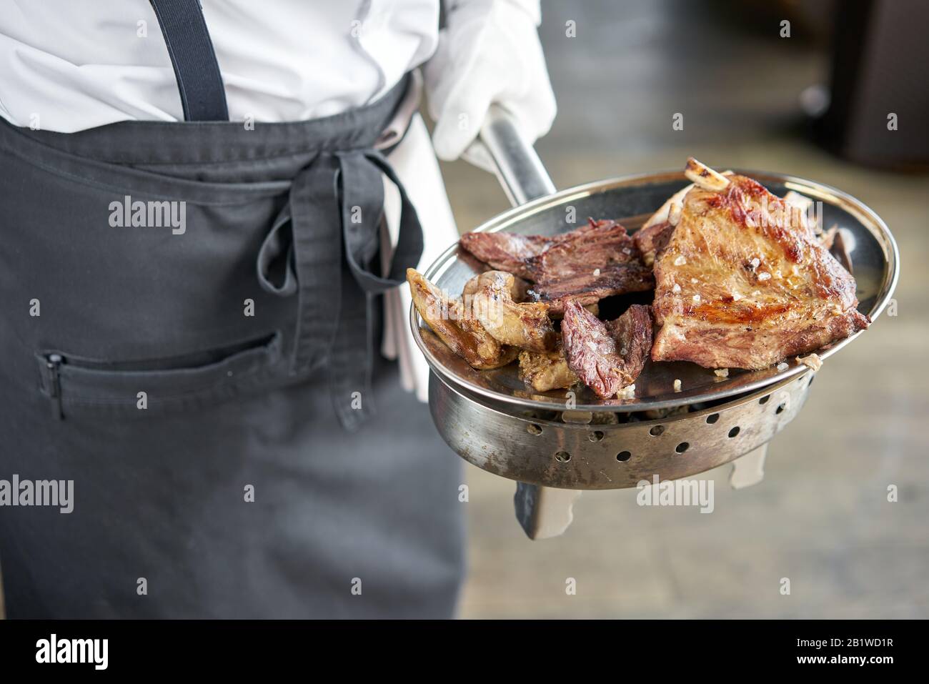 Der Kellner hält einen Teller Mit Verschiedenen gegrillten Fleischgerichten. Grillrestaurant Menü, eine Reihe von Fotos von verschiedenen Fleischsorten. Stockfoto