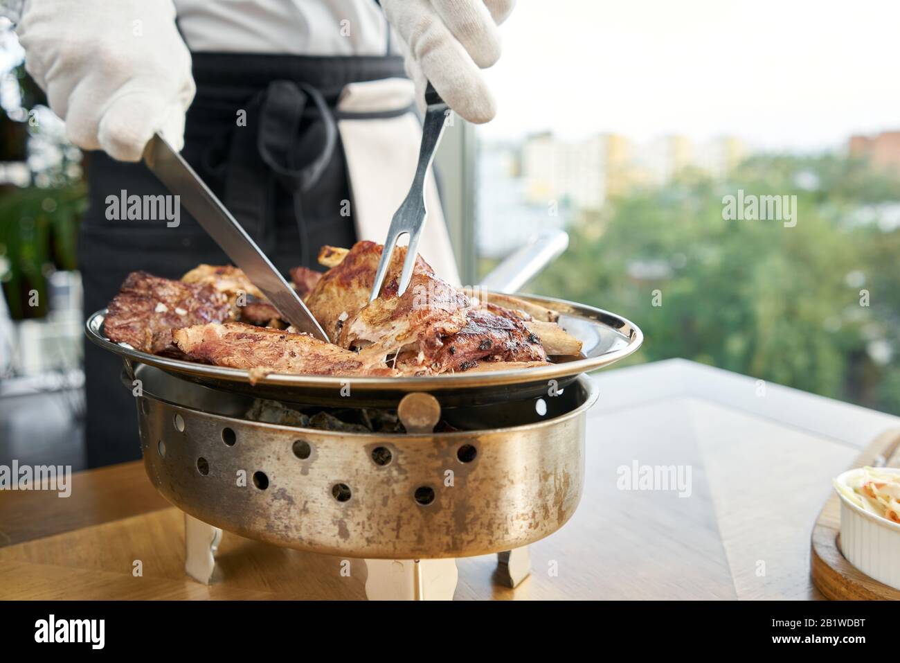 Der Kellner knutschelt mit einem Messer. Verschiedene gegrillte Fleischgerichte. Grillrestaurant Menü, eine Reihe von Fotos von verschiedenen Fleischsorten. Stockfoto