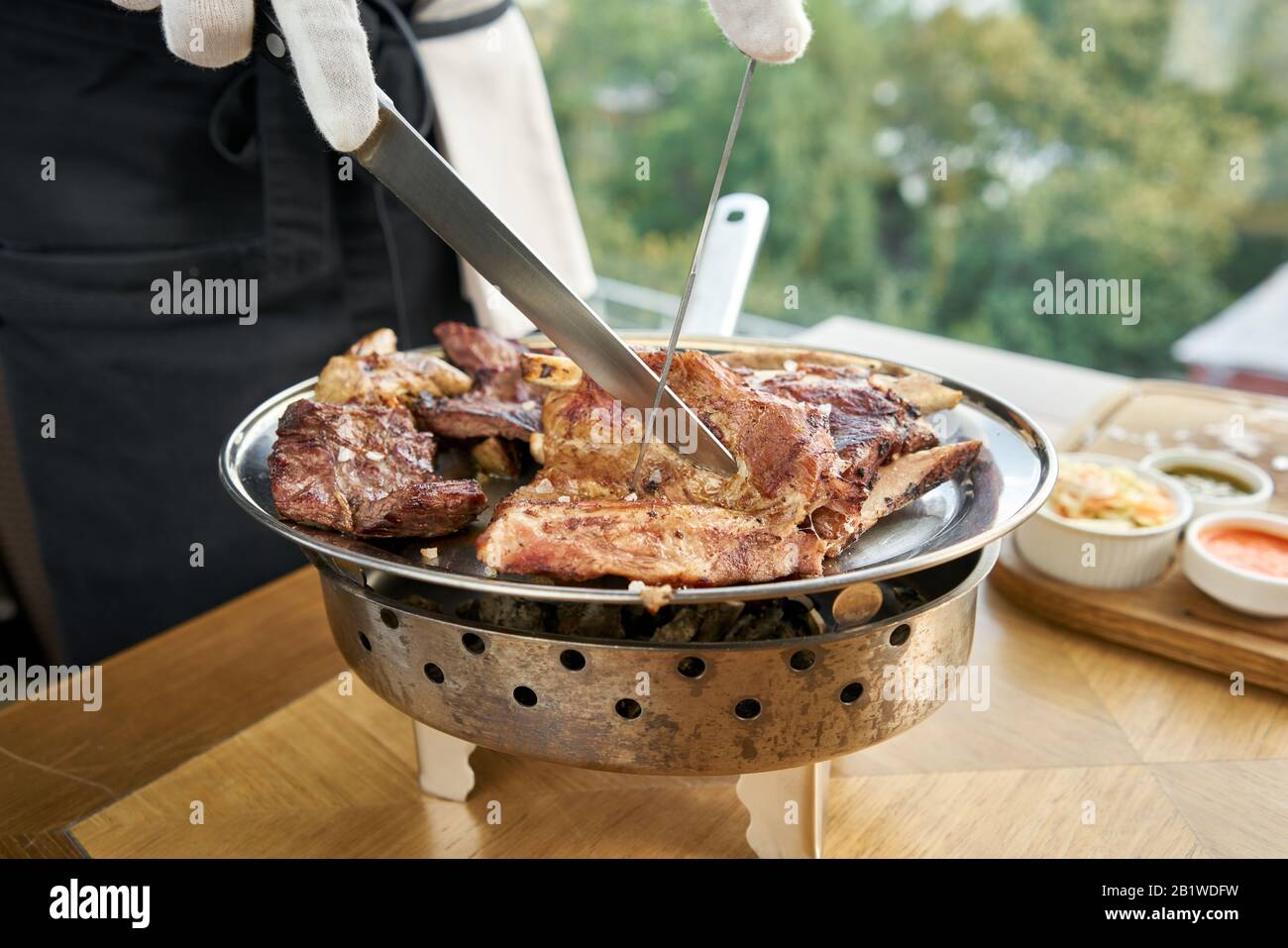 Der Kellner knutschelt mit einem Messer. Verschiedene gegrillte Fleischsorten. Grillrestaurant Menü, eine Reihe von Fotos von verschiedenen Fleischsorten. Stockfoto