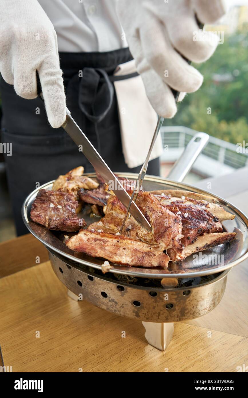Der Kellner knutschelt mit einem Messer. Verschiedene gegrillte Fleischgerichte. Grillrestaurant Menü, eine Reihe von Fotos von verschiedenen Fleischsorten. Stockfoto