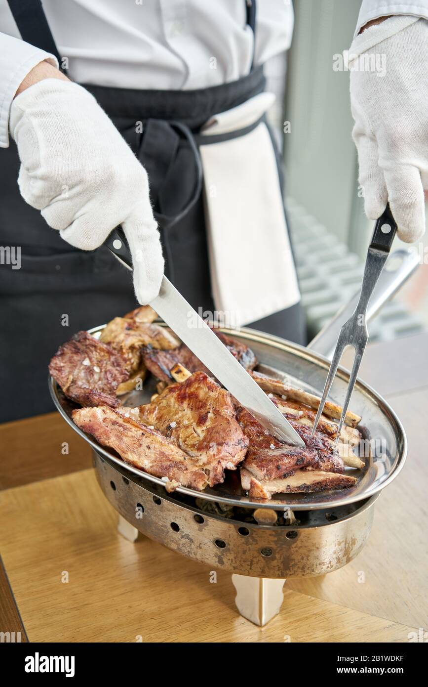 Der Kellner knutschelt mit einem Messer. Verschiedene gegrillte Fleischgerichte. Grillrestaurant Menü, eine Reihe von Fotos von verschiedenen Fleischsorten. Stockfoto