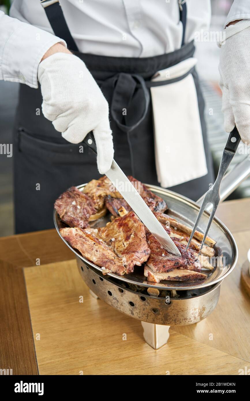 Der Kellner knutschelt mit einem Messer. Verschiedene gegrillte Fleischsorten. Grillrestaurant Menü, eine Reihe von Fotos von verschiedenen Fleischsorten. Stockfoto
