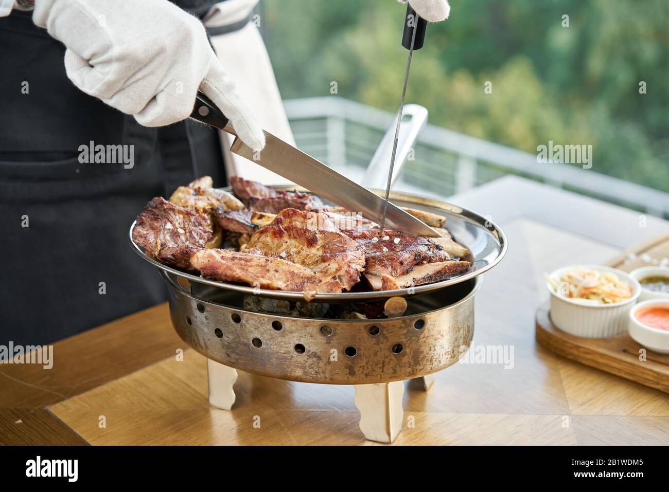 Der Kellner knutschelt mit einem Messer. Verschiedene gegrillte Fleischgerichte. Grillrestaurant Menü, eine Reihe von Fotos von verschiedenen Fleischsorten. Stockfoto