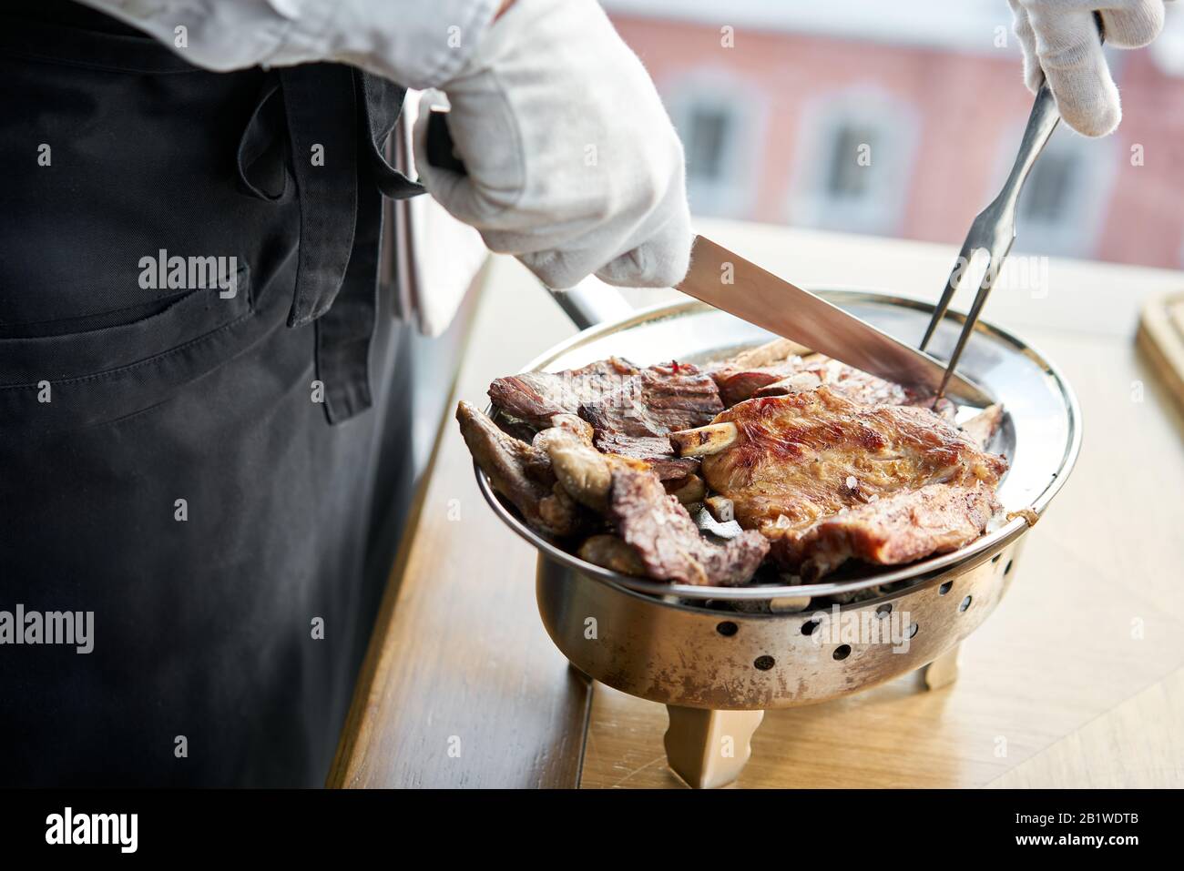 Der Kellner knutschelt mit einem Messer. Verschiedene gegrillte Fleischgerichte. Grillrestaurant Menü, eine Reihe von Fotos von verschiedenen Fleischsorten. Stockfoto
