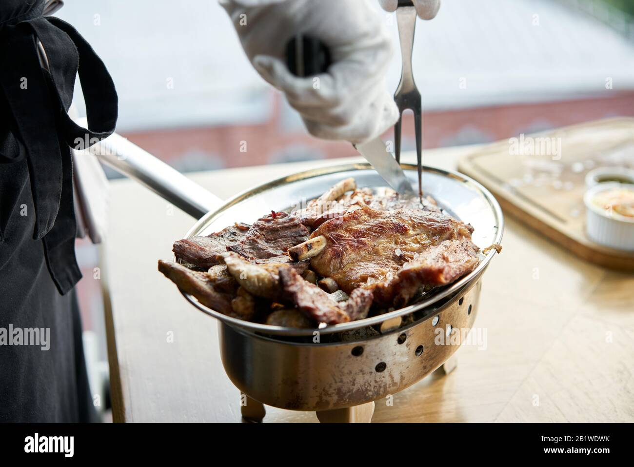 Der Kellner knutschelt mit einem Messer. Verschiedene gegrillte Fleischgerichte. Grillrestaurant Menü, eine Reihe von Fotos von verschiedenen Fleischsorten. Stockfoto