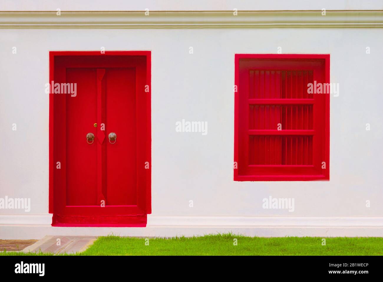 Intensiv blutrot bemalte Tür und Fenster an einer weißen Wand. Gesättigte, auffällige Farbe, kontrastreiche Bilder. Stockfoto