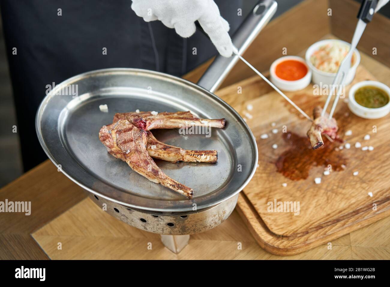 Der Kellner ist Schlachten mit einem Messer. Lammrücken, gegrilltes Fleisch mit Knochen. Grill Restaurant Menü, eine Reihe von Fotos von verschiedenen Fleischsorten Stockfoto