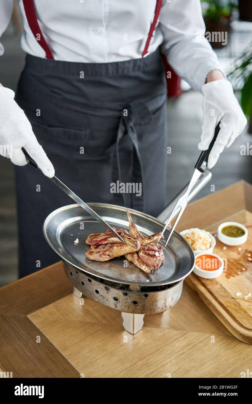 Der Kellner ist Schlachten mit einem Messer. Lammrücken, gegrilltes Fleisch mit Knochen. Grill Restaurant Menü, eine Reihe von Fotos von verschiedenen Fleischsorten Stockfoto