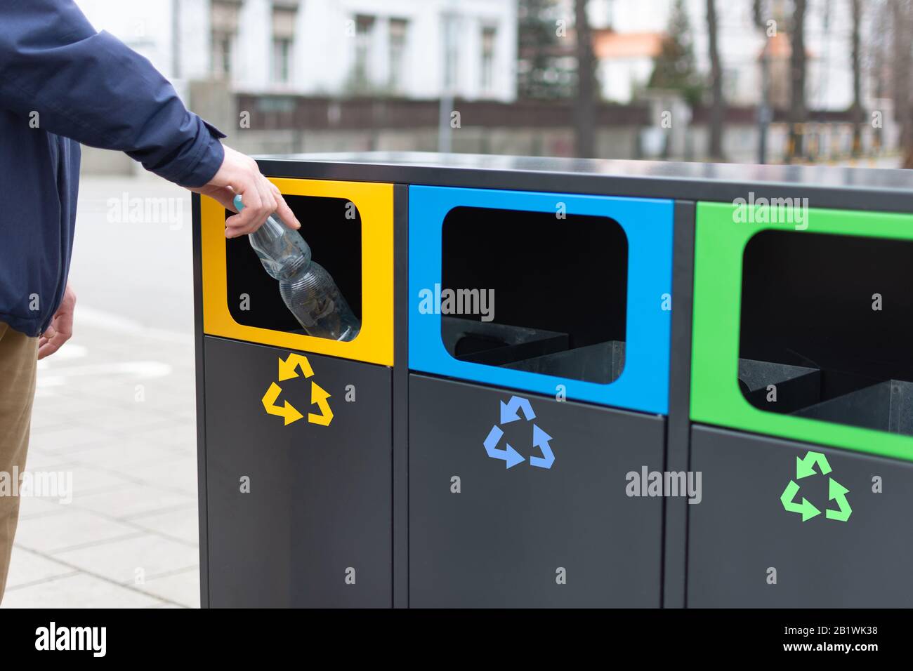 Die Hand des Mannes, der die Plaztic-Flasche in den Papierkorb wirft, um Plastikmüll zu verschwenden. Moderne bunte Mülltonnen für separaten Müll. Umweltbewusstsein ist lebendig Stockfoto