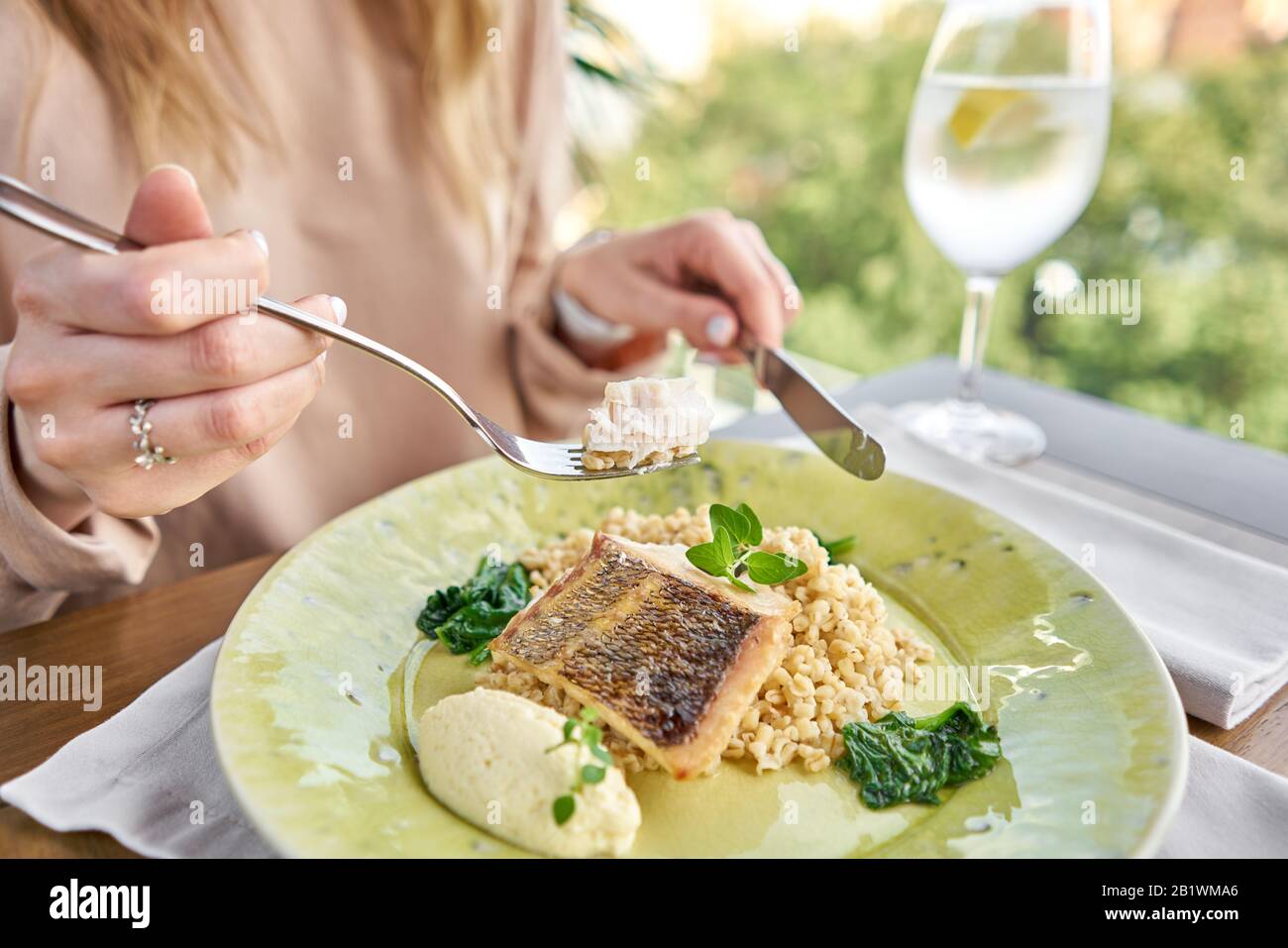 Gebratenes Zanderfilet mit Dinkel und polnische Soße. Mittagessen im Restaurant, eine Frau isst Lecker und gesund Essen. Teller mit Spinat eingerichtet Stockfoto