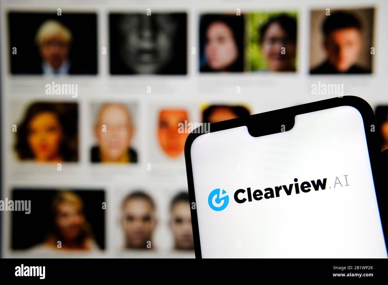 Das Firmenlogo von Clearview AI auf dem Smartphone-Bildschirm hält sich mit verschwommenen Gesichtern im Hintergrund in den Händen. Konzeptfoto für Gesichtserkennungssoftware. Stockfoto