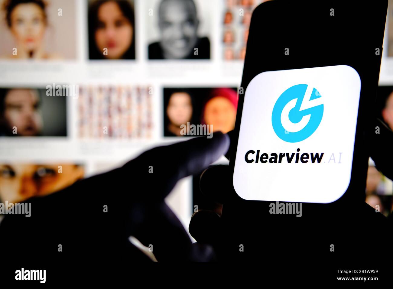 Das Firmenlogo von Clearview AI auf dem Smartphone-Bildschirm hält sich mit verschwommenen Gesichtern im Hintergrund in den Händen. Konzeptfoto für Gesichtserkennungssoftware. Stockfoto