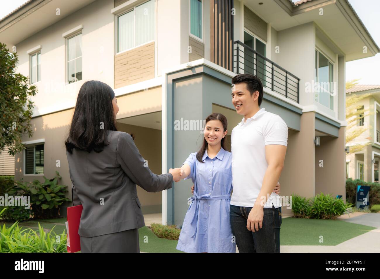 Asian Happy Smile junge Paare geben sich nach Vertragsabschluss mit Immobilienmakler oder Realtor vor ihrem Haus ein, Konzept für Real Stockfoto