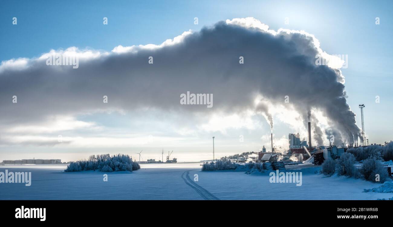 Blick auf das Fabrikkraftwerk im Winter mit Dampf, der in tiefblauen Himmel steigt, Seehafen mit dem Boot, viele Öltanks und zwei Windmühlen an der Horizont-Linie Stockfoto