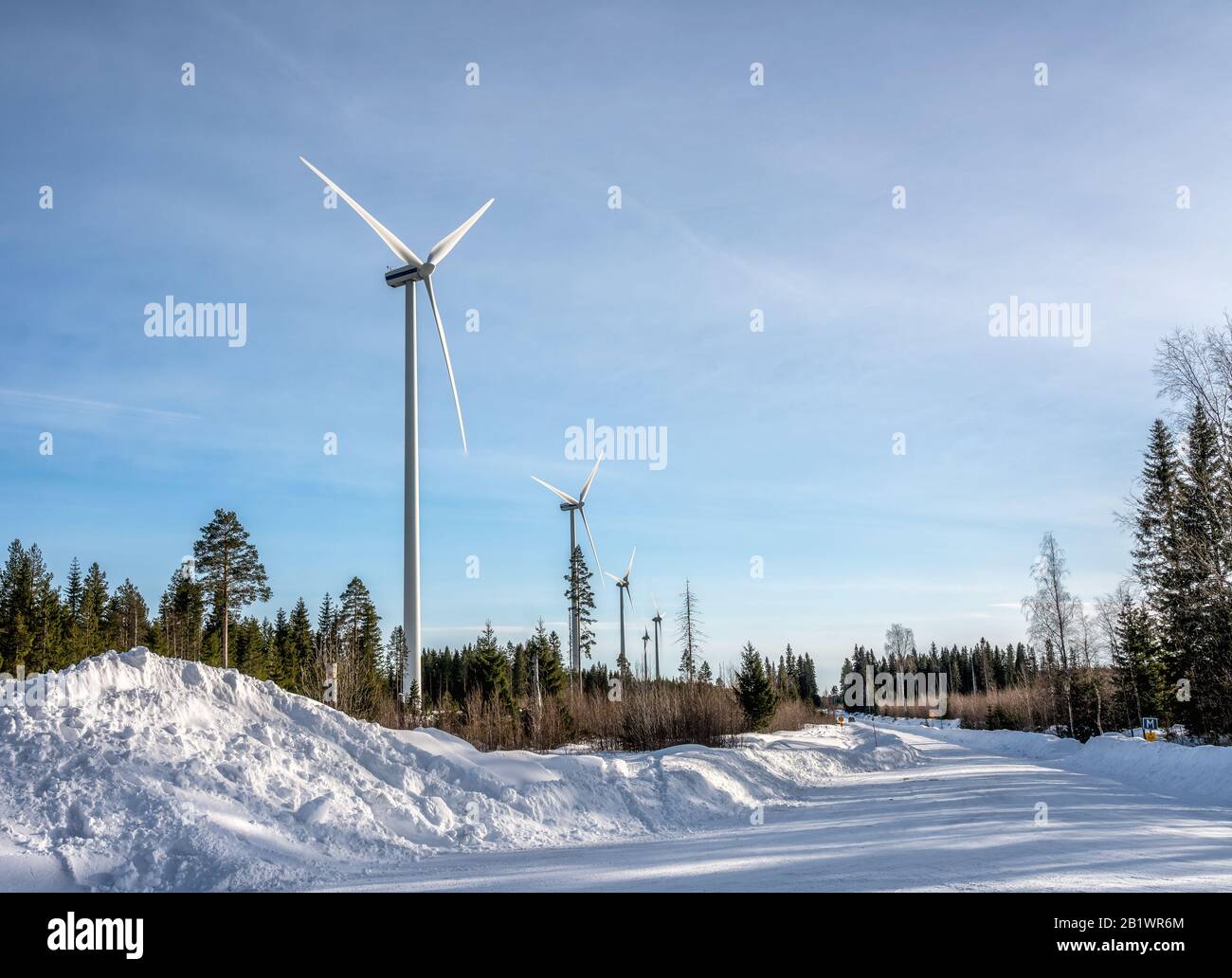 Foto von Windmühlenfarm und geraden Straße im Winterwald, blauer Himmel, sonnig, umweltfreundlich grüne ökologische Energieerzeugung Stockfoto