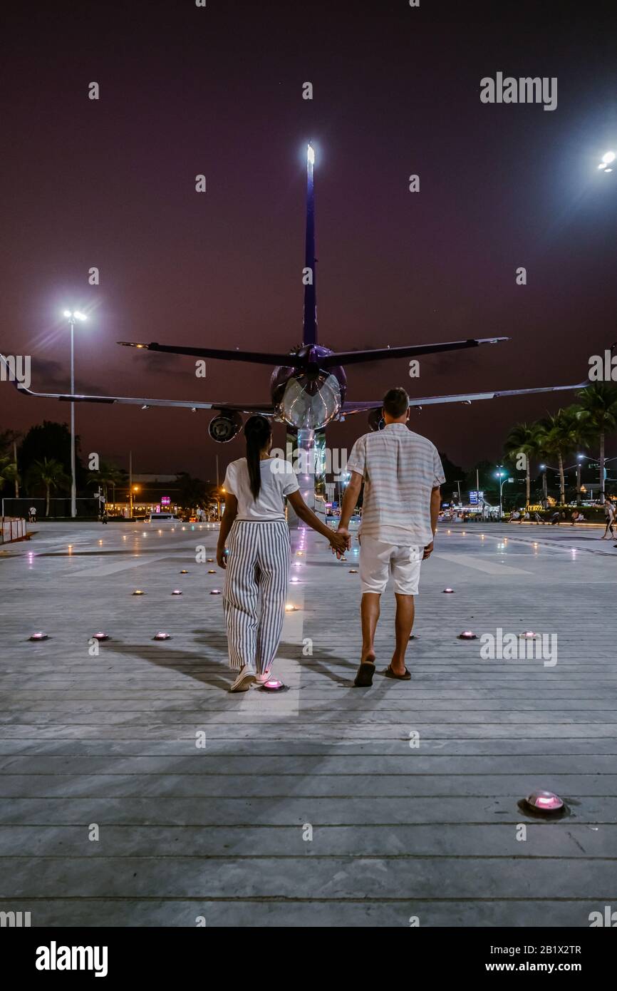 Ein Paar, das auf der Straße in Thailand mit dem Flugzeug auf dem Hintergrund spazieren geht, Pattaya Thailand Sonnenuntergang Stockfoto