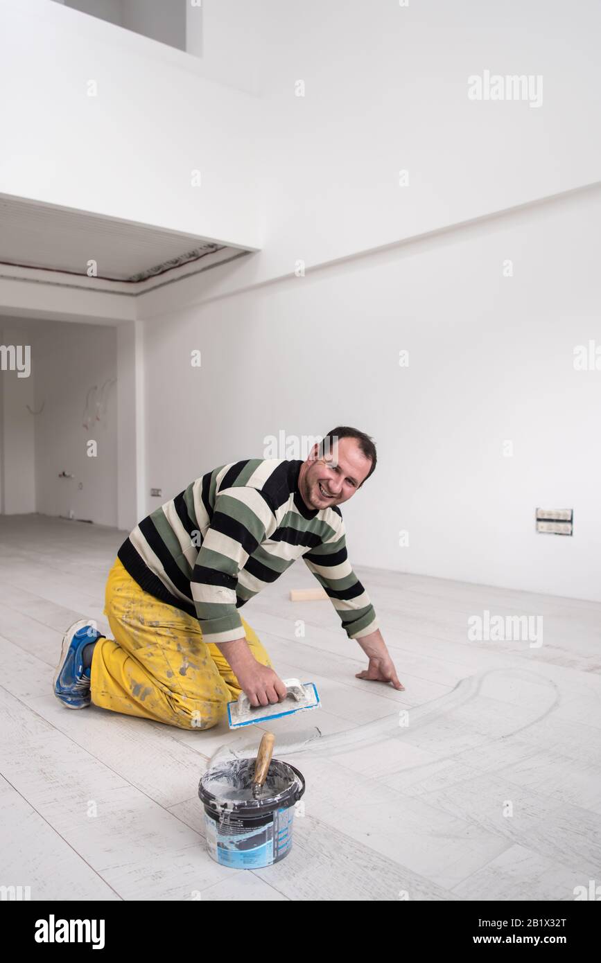 Verfugen von Keramikfliesen. Tiler füllen den Raum zwischen Keramikfliesen aus Holz mit einem Gummi-Trowel auf dem Boden in einer neuen modernen Wohnung Stockfoto