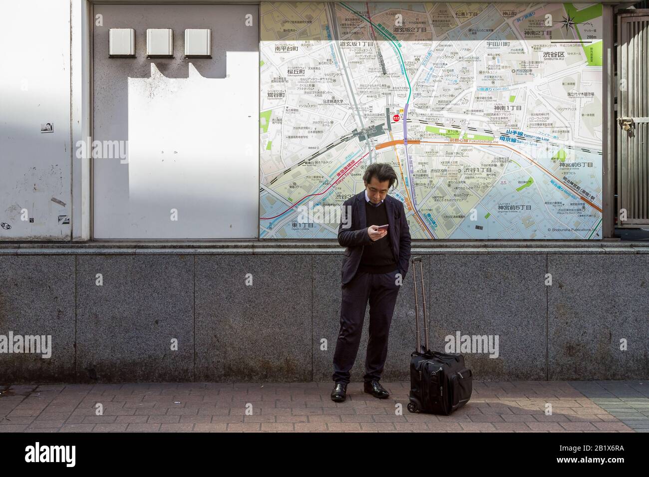 Ein Japaner überprüft sein Smartphone vor einer Karte der Region Shibuya. Hachiko Square, Shibuya, Tokio, Japan, Stockfoto